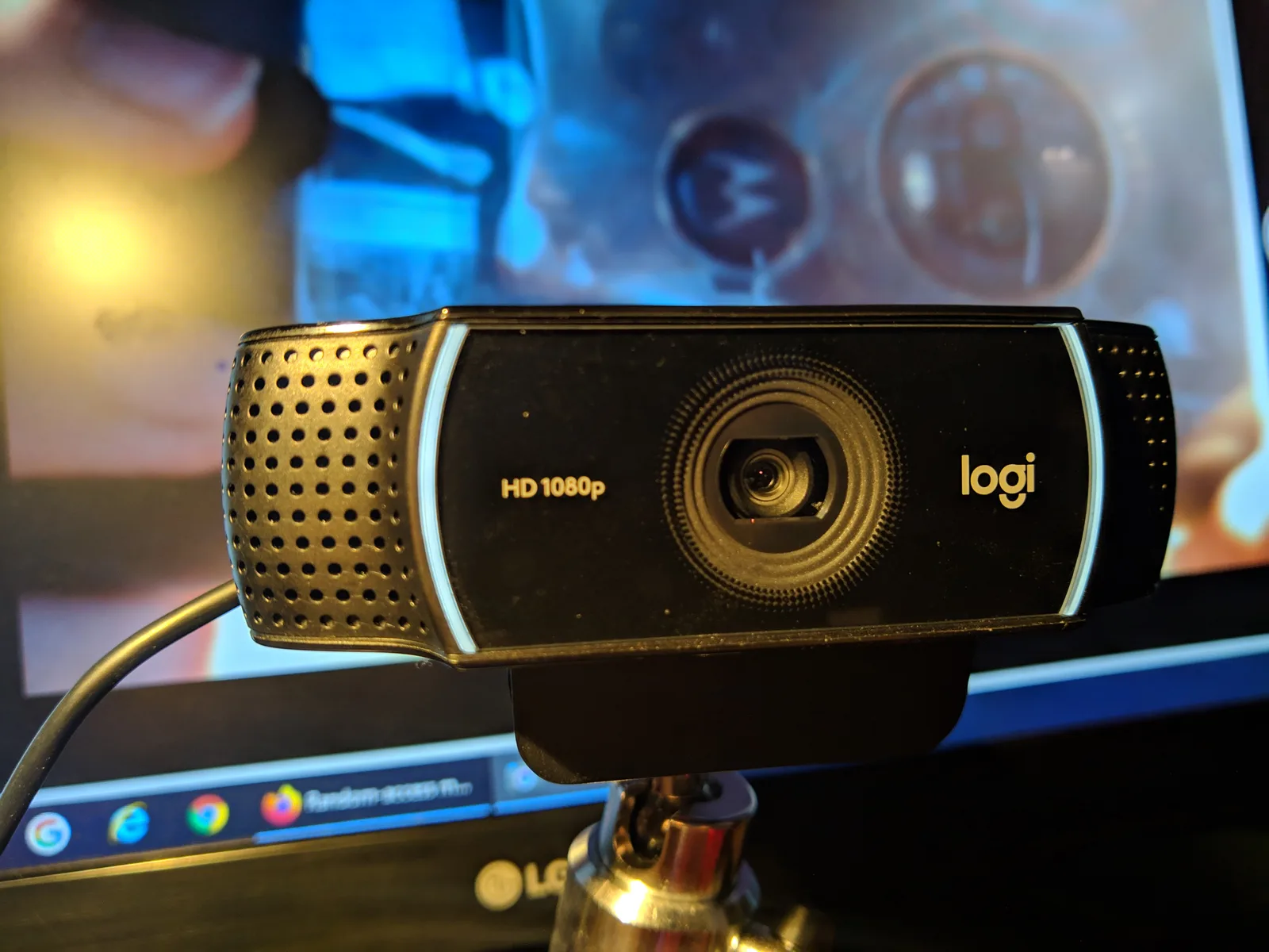 A Logitech C922 webcam mounted on top of a monitor, lit by warm desk light