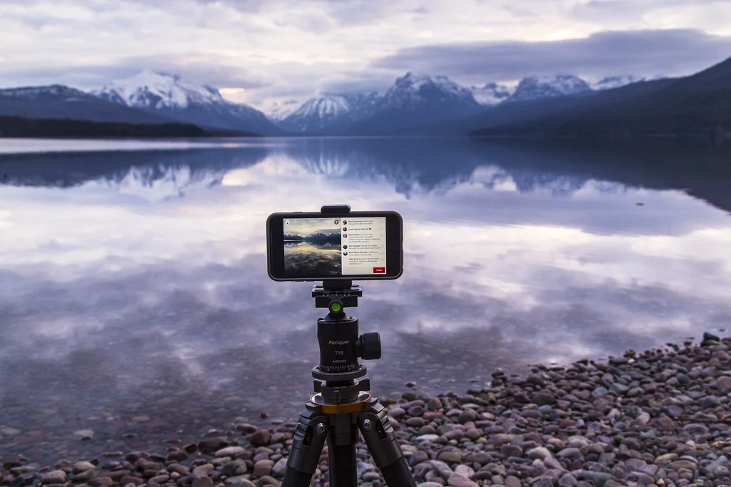A smartphone mounted on a small tripod, live-streaming a mountain lake at sunrise